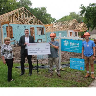 A woman and three men standing in front of partially constructed houses, holding a giant check.