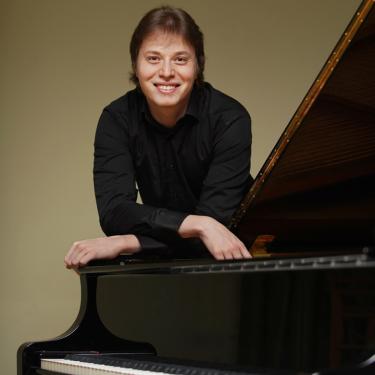 Photo of Ilya Shmukler leaning on grand piano