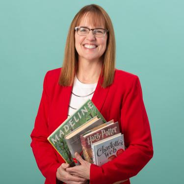 Photo of Susan Wray wearing red sport coat, holding books.