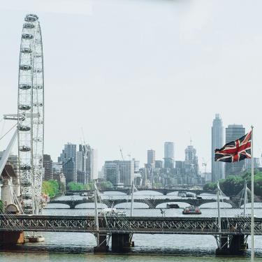 Photo of London Eye near British Flag with city skyline in background.